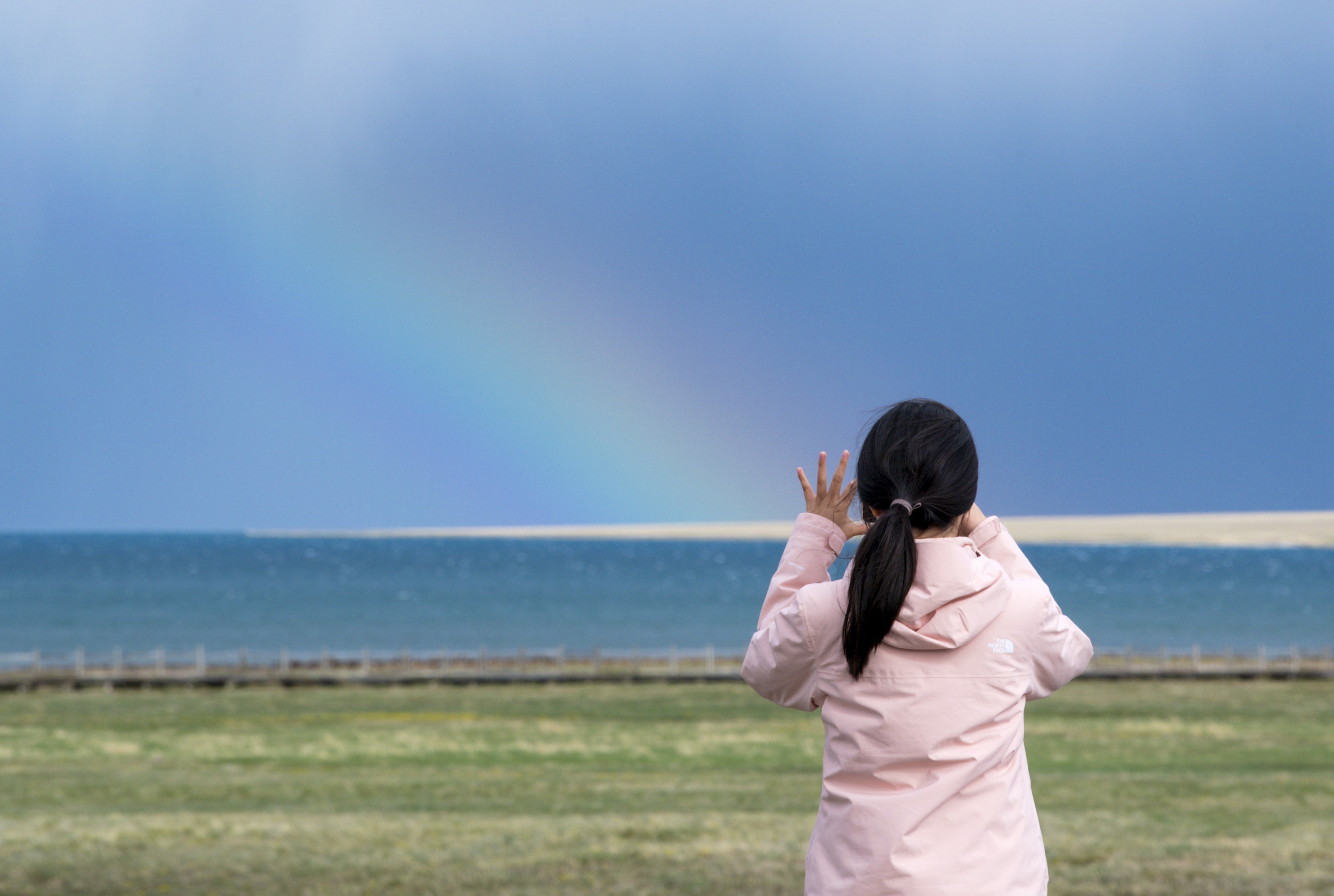 游客在赛里木湖边拍摄彩虹（5月21日摄）。（摄影：新华社记者王菲）